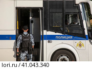 Сотрудник ОМОН заходит в специальный полицейский автомобиль для перевозки задержанных на публичных акциях, в центре города Москвы, Россия (2023 год). Редакционное фото, фотограф Николай Винокуров / Фотобанк Лори