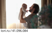 Young neo father is playing with his newborn baby in a nursery morning. Father's Day. Father holds in hands little Child and Plays with him. Concept of children, baby, parenthood, childhood, family. Стоковое видео, видеограф Марина Демидюк / Фотобанк Лори