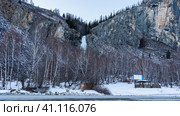 A frozen waterfall is visible in the gorge between the mountain slopes. On the side of the road, in the snowdrifts there is a gazebo, bare trees. Altai. Стоковое фото, фотограф Вера Ивановна Кубарева / Фотобанк Лори