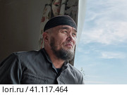 Portrait of senior asian man with beard wearing skullcap sitting by window. Стоковое фото, фотограф Ирина Кононова / Фотобанк Лори