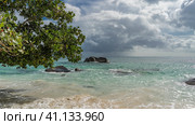 Granite boulders rise in the turquoise ocean. The waves are foaming at the shore. The branches of tropical trees hang over the water. Blue sky, clouds. Seychelles. Стоковое фото, фотограф Вера Ивановна Кубарева / Фотобанк Лори