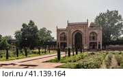 The building in the complex Tomb of Itimad-ud-Daulah is built of red sandstone and decorated with white ornaments. Visible arches, dome. Green vegetation grows on the sides of the paved path. India. (2022 год). Стоковое фото, фотограф Вера Ивановна Кубарева / Фотобанк Лори
