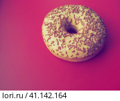 A doughnut or donut. A type of leavened fried dough. Sweet snack that can be homemade or purchased in bakeries, supermarkets, food stalls. Delicious pie with light icing on a crimson background. Стоковое фото, фотограф Юлия Петровская / Фотобанк Лори