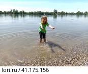 The girl stands knee-deep in the water and stretches her arms forward. A child at the pond. A girl with long white hair smiles and plays with drops and splashes. Serbia, Sava River, Sremska Mitrovica. Стоковое фото, фотограф Юлия Петровская / Фотобанк Лори