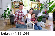 Traditional family with child are enjoying new home, sitting on the sofa and holding the roof. Mortgage, insurance and protection, buying and moving into your own home, green house with potted plant. Стоковое видео, видеограф Ольга Симонова / Фотобанк Лори