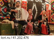 Moscow, Russia - September 15, 2019: Traditional atmosphere, bright home furniture, decoration in Bashkiria. Old lifestyles, fashion at home. Floral pattern of carpet. Family play squeezebox and kubyz. Редакционное фото, фотограф YuryKara / Фотобанк Лори