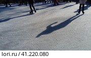 Children ride in a city park on an ice rink. Feet skater while skating on ice. The low winter sun weakly illuminates the ice. Dark shapes and long shadows on the surface. Sports movements. Стоковое фото, фотограф Юлия Петровская / Фотобанк Лори