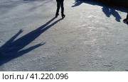 Children ride in a city park on an ice rink. Feet skater while skating on ice. The low winter sun weakly illuminates the ice. Dark shapes and long shadows on the surface. Sports movements. Стоковое фото, фотограф Юлия Петровская / Фотобанк Лори