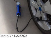 Blue automobile compressor is standing next to the car wheel. Electric pump inflates the flat tire. Top view. Focus on the manometer. Синий автомобильный компрессор стоит рядом с колесом автомобиля. Электрический насос накачивает спущенную шину. Вид сверху. Стоковое фото, фотограф Дмитрий Березнев / Фотобанк Лори