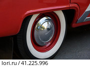 Closeup photo of the rear wheel of a magnificent retro car. The wheel has a red stamped disc in the body color, a large chrome hood and white wall. Фотография заднего колеса великолепного ретро-автомобиля крупным планом. Колесо имеет красный штампованный диск в цвет кузова, большой хромированный колпак и белую каемку. Стоковое фото, фотограф Дмитрий Березнев / Фотобанк Лори