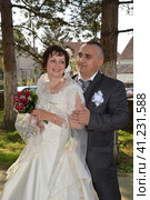 The bride holds a bouquet of red roses in her hands and smiles. The groom in a suit looks at the bride and smiles. Man holds a woman's arm. Стоковое фото, фотограф Юлия Петровская / Фотобанк Лори