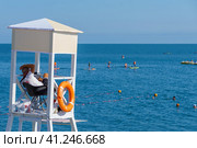 Спасатель на вышке наблюдает за купающимися людьми в Черном море, чтобы не заплывали за буйки. Пляж на Имеретинском курорте в Сочи в жаркий летний день (2023 год). Редакционное фото, фотограф Sergei Gorin / Фотобанк Лори