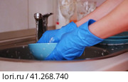 A girl in blue gloves washes a deep plate with a soapy sponge under running water. Стоковое видео, видеограф Алексей Гекало / Фотобанк Лори