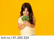 Little cute kid girl refusing to eat healthy vegetables broccoli on yellow background. Children do not like to eat vegetables. Стоковое фото, фотограф Ирина Михайличенко / Фотобанк Лори