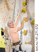 positive muscular retired woman in gym climbing up artificial rock climbing wall. Стоковое фото, фотограф Яков Филимонов / Фотобанк Лори