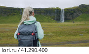 Woman with backpack looking at Seljalandsfoss waterfall Iceland. Стоковое видео, видеограф Igor Tichonow / Фотобанк Лори