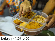Hand holding additions as cookies, nuts for ice cream in coconut shell in Jalan Alor street food market in Kuala Lumpur (2023 год). Стоковое фото, фотограф Татьяна Терехина / Фотобанк Лори