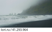 The black sand beach of Reynisfjara with waves hitting the shore on foggy rainy stormy day Vik, Icel. Стоковое видео, видеограф Igor Tichonow / Фотобанк Лори