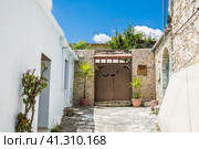 Stony alleyway and entrance to the house in Lefkara, Cyprus. Gates decorated with plants in pots over the background of blue sky. Welcome plate on the wall. Каменистая аллея и вход в дом в Лефкаре, Кипр. Ворота украшены растениями в горшках на фоне голубого неба. Приветственная табличка на стене (2019 год). Стоковое фото, фотограф Дмитрий Березнев / Фотобанк Лори