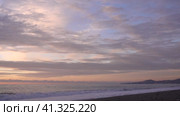 Evening. Sea. The sky is painted in pastel shades of pink and blue. The cape and city buildings are visible in the distance. Waves foaming on a pebble beach. A husky dog runs along the shore and hides. Стоковое видео, видеограф Вера Ивановна Кубарева / Фотобанк Лори