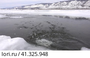 Early spring. On the frozen Lake Baikal, there is a polynya in which ice floes float. Suddenly a piece of ice falls into the water, large transparent splashes. The background is a snowy mountain range. Стоковое видео, видеограф Вера Ивановна Кубарева / Фотобанк Лори