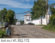 Девушка-художник, накрывшись черным зонтом, работает над  этюдом у стены Троицкого Данилова мужского монастыря в Переславле-Залеском в солнечный летний день (2023 год). Редакционное фото, фотограф Наталья Николаева / Фотобанк Лори