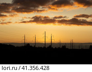 Silhouettes of power poles against background of an orange sunset sky and floating clouds (2023 год). Стоковое фото, фотограф Попова Ольга / Фотобанк Лори