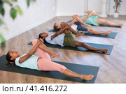 Children doing yoga with group in studio, lying on mat with knee pressed to chest with hands, performing hamstring and low back stretching Ardha Pawanmuktasana. Стоковое фото, фотограф Яков Филимонов / Фотобанк Лори