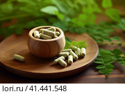Wooden bowl of moringa capsules and fresh leaves on the table. Superfood, dietary supplement. AI generated. Стоковое AI-изображение, AI-художник Александра Селина / Фотобанк Лори