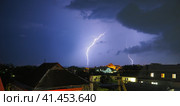 Two lightning bolts against the background of a dark sky with clouds. Thunderstorm over the city. Discharges of thunder and lightning over the rooftops. Thunderstorm front, typhoon or cyclone. Стоковое фото, фотограф Юлия Петровская / Фотобанк Лори
