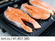 Three raw salmon steaks are toasted on a modern electric non-stick coating grill. Healthy eating concept. Три стейка из сырого лосося поджариваются на современном электрическом гриле с антипригарным покрытием. Концепция здорового питания. Стоковое фото, фотограф Дмитрий Березнев / Фотобанк Лори