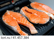 Three raw salmon steaks are toasted on a modern electric non-stick coating grill. Healthy eating concept. Close up photo with selective focus. Три стейка из сырого лосося поджариваются на современном электрическом гриле с антипригарным покрытием. Концепция здорового питания. Фотография крупным планом с выборочным фокусом. Стоковое фото, фотограф Дмитрий Березнев / Фотобанк Лори
