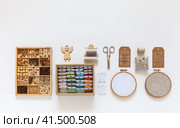 Concept of hand embroidery and crafts. Accessories for cross stitch and bead embroidery: hoops, scissors, set of needles, box with wooden beads, skeins of colorful threads mouline on bobbins in box. Стоковое фото, фотограф Виктория Катьянова / Фотобанк Лори