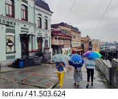 People with bright umbrellas walk through city with old buildings. Rain weather in summer. Beautiful architecture. Admiral Fokin Street, descent to Flower Passage. Vladivostok, Russia, August 10, 2023. Редакционное фото, фотограф Ирина / Фотобанк Лори
