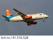 Летящий самолет Сухой SuperJet 100-95B "Иртыш" (RA-89095) авиакомпании "Азимут" в сером облачном небе (2023 год). Редакционное фото, фотограф Виктор Карасев / Фотобанк Лори