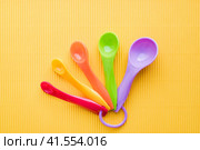 Мерные ложки на желтом фоне. Разноцветные пластиковые мерные ложки. Measuring spoons on a yellow background. Multi-colored plastic measuring spoons. Стоковое фото, фотограф Ольга Митряева / Фотобанк Лори