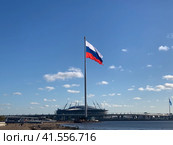 Развевающийся Государственный флаг Российской Федерации (Флаг России)  на фоне Газпром Арены и голубого неба с облаками. Вид с пляжа парка 300-летия Санкт-Петербурга. (2023 год). Стоковое фото, фотограф Елена Яворская / Фотобанк Лори