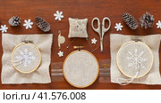 Video of handmade gifts for Christmas. Embroidery of beautiful snowflakes on natural canvas in hoop with white thread. Accessories for embroidery and fir cones nearby on wooden background. Стоковое видео, видеограф Виктория Катьянова / Фотобанк Лори