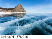 Beautiful winter unusual landscape of frozen Baikal Lake on February sunny day. View from blue ice with cracks of famous sandy beach of Peschanaya bay and  Bell Tower Rock - natural landmark. Стоковое фото, фотограф Виктория Катьянова / Фотобанк Лори