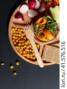 Wooden menagerie with healthy snacks, pieces of fresh vegetables, crispy chickpeas, grain loaves. Close-up on a black background. Стоковое фото, фотограф Bogdanova Mariia / Фотобанк Лори