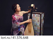A happy female musician in Asian clothes on a studio black background. A smiling woman with a stringed musical instrument from Asia on a dark background. Стоковое фото, фотограф Андрей Журавлев / Фотобанк Лори