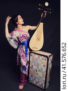 A happy female musician in Asian clothes on a studio black background. A smiling woman with a stringed musical instrument from Asia on a dark background. Стоковое фото, фотограф Андрей Журавлев / Фотобанк Лори