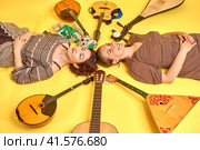 Women musicians in dresses with musical instruments on a yellow studio background. Happy artists with stringed musical instruments with smiles on faces. Стоковое фото, фотограф Андрей Журавлев / Фотобанк Лори
