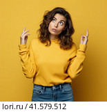 A young, pensive, insecure, rather attractive European girl of 20 years in a yellow casual blouse, spreads her hands questioningly, looking away. Created by AI. Стоковое AI-изображение, AI-художник Ярославский Максим / Фотобанк Лори