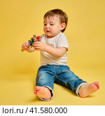 Toddler baby plays with a musical rattle bells on a stick, studio yellow background. Happy child musician playing percussion musical instrument. Kid aged one year four months. Стоковое фото, фотограф Андрей Журавлев / Фотобанк Лори