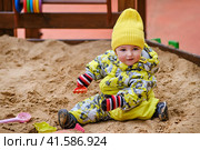 Happy toddler baby boy is playing in the sandbox. A child in warm clothes is playing with sand on the playground. Kid aged one year and two months in a yellow autumn jumpsuit. Стоковое фото, фотограф Андрей Журавлев / Фотобанк Лори