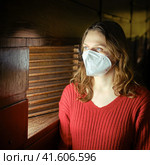 Young woman in medical mask ffp2 respirator looking out the ajar window. Стоковое фото, фотограф Андрей Журавлев / Фотобанк Лори