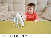 Playing with a hot iron in the living room without supervision is putting both the baby and child at risk of getting burned or hurt. Kid aged about two years (one year ten months) Стоковое фото, фотограф Андрей Журавлев / Фотобанк Лори