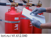 The inspector of fire security is using his notepad to jot down notes as he checks the fire extinguishers within the building. Стоковое фото, фотограф Андрей Журавлев / Фотобанк Лори