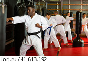 African american man in kimono practicing powerful body punches on heavy punchbag. Стоковое фото, фотограф Яков Филимонов / Фотобанк Лори